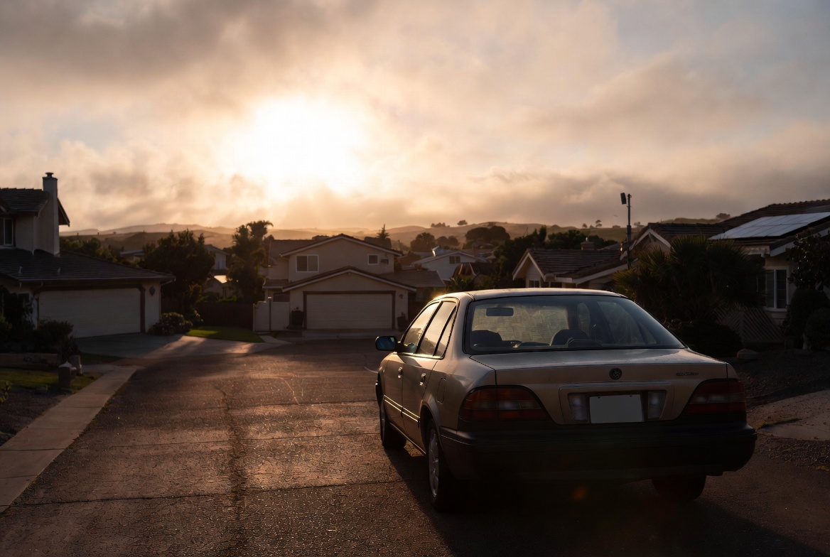 A car parked in a quiet neighborhood at sunset — representing the end of an era of independence