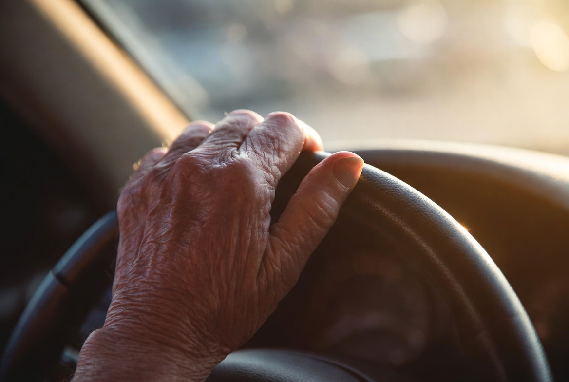 An elderly person's hand on a steering wheel — driving safety and independence in senior years